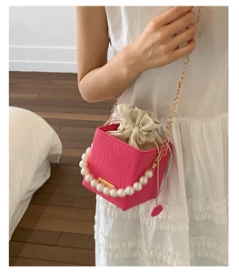 Detail of rose red bucket bag featuring woven texture and white pearl handle detail