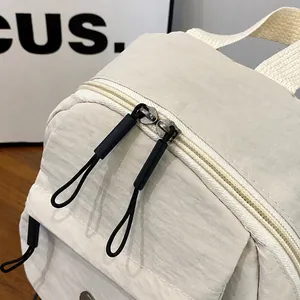 Detailopname van een crèmewitte nylon tas met dubbele metalen ritsen en zwarte trekkoorden