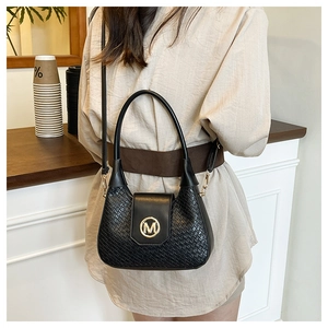 Détail d'un sac à main noir tressé avec boucle dorée en M et fine bandoulière réglable