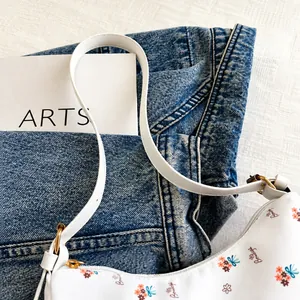 Detalle de bolso floral blanco con asa elegante de cuero y herrajes dorados