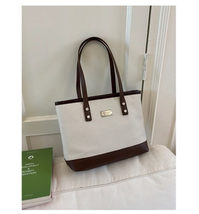 Détail du sac cabas tissé en tissu beige avec base en cuir marron et logo argenté
