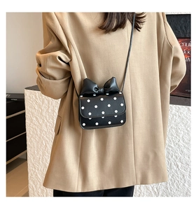Close-up of black polka dot crossbody bag with a large bow detail and long strap