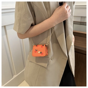 Close-up of orange mini crossbody bag with strawberry print and gold chain strap