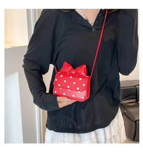 Close-up of red polka dot crossbody bag featuring a large decorative bow on the top flap
