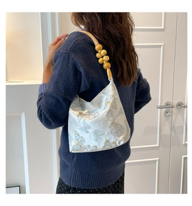 Détail de broderie papillon sur sac en satin blanc avec poignée en perles de bois