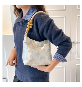 Détail de la texture brodée papillon et de l'anse en perles de bois sur le sac à main