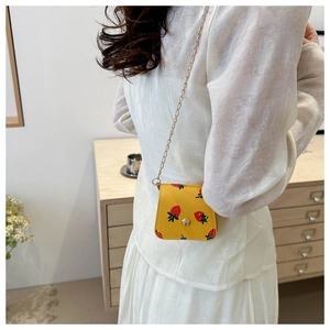 Detailed view of yellow mini crossbody bag with strawberry print and gold chain strap