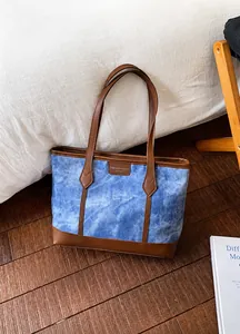 Detail of denim blue tote bag with brown leather trim in cozy lifestyle setting