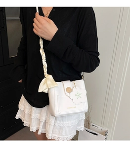 Detail of white bucket bag with floral pendant and silk ribbon bow on the shoulder strap