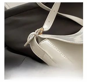 Detail view of white patent leather shoulder bag with gold buckle and precise stitching