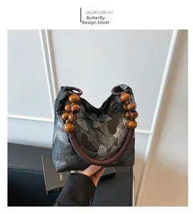 Détail de la broderie papillon argentée sur tissu gris avec anse en perles de bois