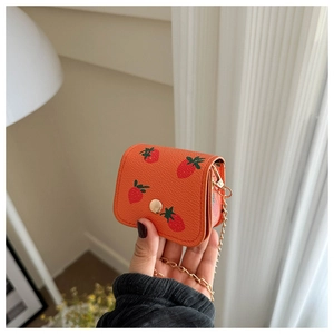 Détail du mini sac orange à imprimé fraise avec texture grainée et chaîne dorée