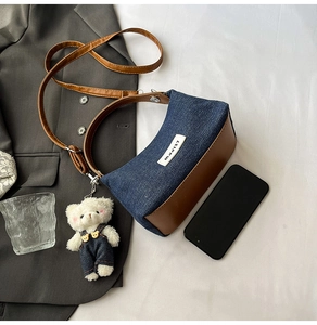 Close-up of blue denim and brown leather crossbody bag with cute bear charm and strap