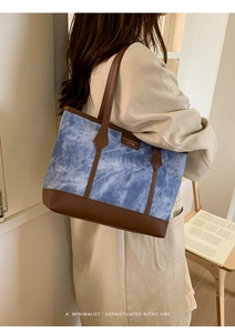 Close-up of blue tie-dye canvas tote bag with brown leather trim and fashion tag detail