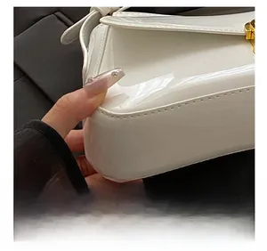 Detail of white patent leather handbag showing precise stitching and golden metal buckle