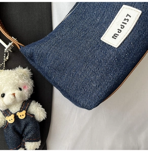 Detail of dark blue denim shoulder bag with leather strap and plush bear charm