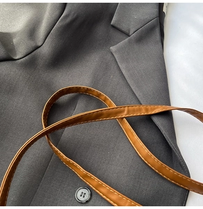 Detail of brown leather strap with yellow stitching on dark grey blazer fabric