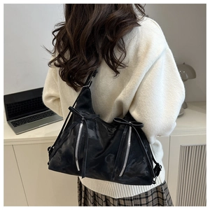 Detail of black tote bag with silver zippers and bow ribbons worn by a model