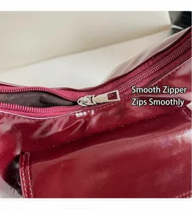 Close-up of a burgundy patent leather handbag featuring a smooth silver metal zipper detail