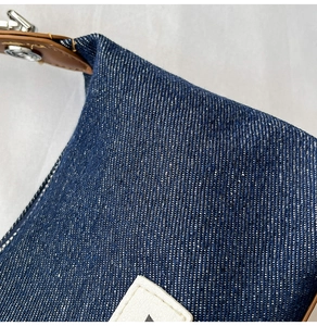 Detail of dark blue denim bag with brown leather strap and white 'F' patch
