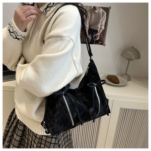 Detail of black bow shoulder bag showing shiny satin texture on model in warm interior