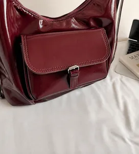 Detail of burgundy patent leather handbag with silver buckle and front flap pocket