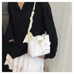 Detail of white PU bucket bag with silk scarf strap decoration and flower pendant