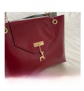 Close-up of wine red glossy shoulder bag with gold deer pendant and chain strap detail
