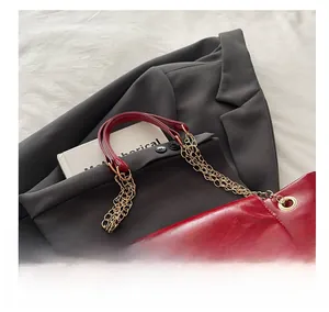 Close-up of red textured leather tote bag with gold chain strap on grey blazer