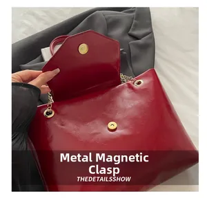 Detail of burgundy glossy leather shoulder bag featuring a gold magnetic snap closure