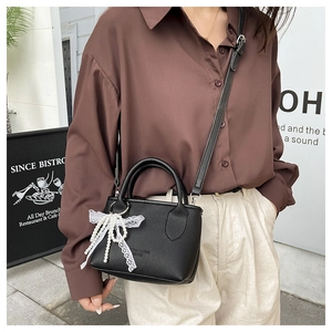 Detail of black lychee leather mini tote with pearl lace bow charm on model's outfit