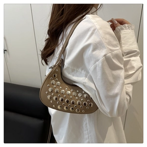 Close-up of khaki crescent bag with silver rivets worn by a model in a modern room