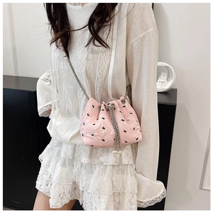 Pink drawstring bucket bag with pearl accents and metal chain strap on model