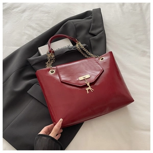 Close-up of deep red glossy tote bag featuring golden deer charm and chain strap detail