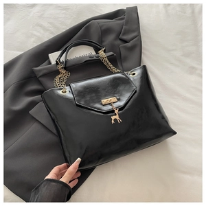 Detail of black glossy PU leather tote bag with gold chain and deer pendant on grey blazer