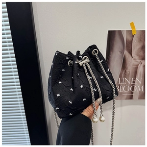 Detail of black drawstring bucket bag with white bows and elegant pearl charms