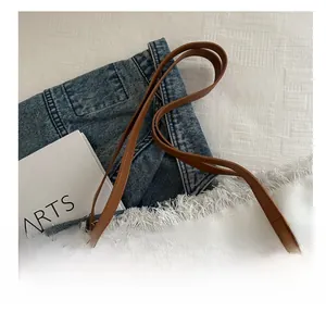 Détail du sac cabas en toile blanche avec anses en cuir marron et pompons décoratifs