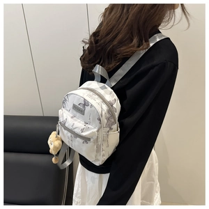 Détail d'un mini sac à dos blanc avec imprimés papillons et breloque ours en peluche