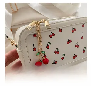 Close-up of white crossbody bag with cherry prints and a golden cherry pendant charm