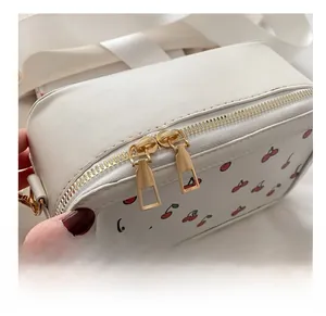 Detail showing smooth gold metal double zippers on white cherry print crossbody bag