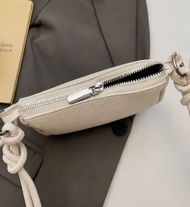 Nahaufnahme der beigen Tasche mit Litschi-Struktur, silbernem Reißverschluss und Knotengurt