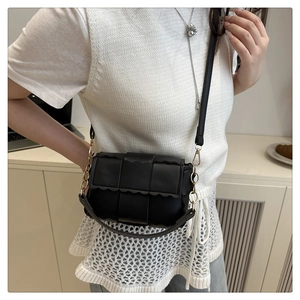 Détail d'un sac bandoulière tissé noir avec rabat festonné et chaîne en métal doré