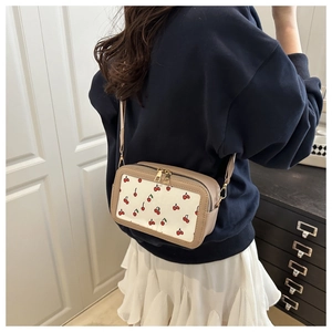 Detail of crossbody bag with cherry print, golden zippers and beige side panels