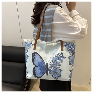Detail of light blue canvas tote bag with butterfly embroidery and white fringe trim