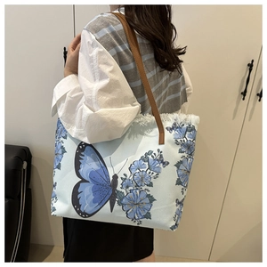 Detail of canvas tote bag featuring blue butterfly embroidery and vintage tassel edges