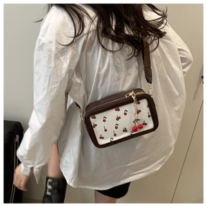 Detail of a square crossbody bag with cherry prints and a wide leather shoulder strap
