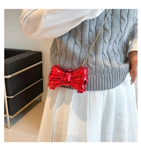 Détail d'un mini sac nœud rouge brillant avec sa fine bandoulière en chaîne dorée