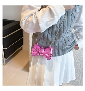 Mini metallic pink bow shoulder bag with gold chain strap worn by a model