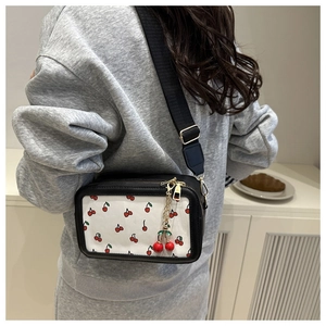 Detail showing the adjustable wide strap and cherry charm on a black and white crossbody bag