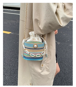 Close-up of a striped woven bucket bag with pearl accent and chain strap on a trench coat